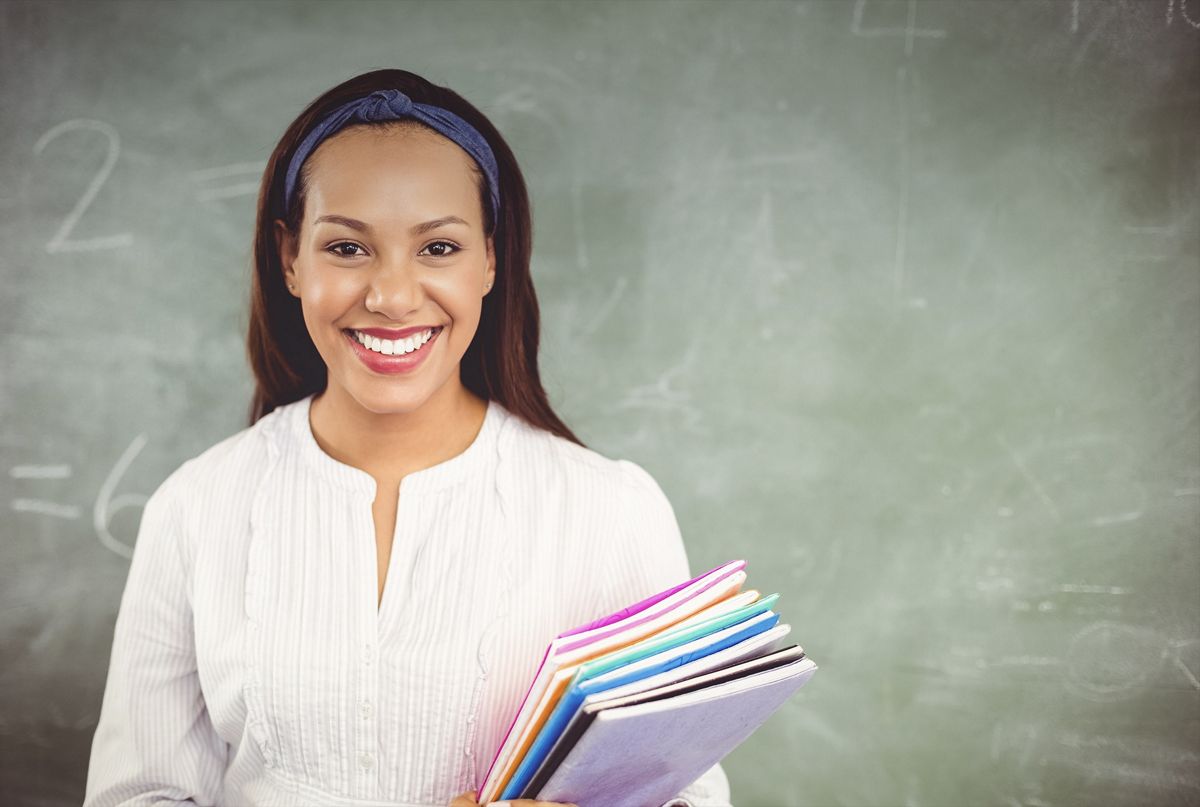 Teacher holding books in front of a chalkboard read to start her professional development courses